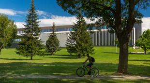 Un estudiante circula por el campus de la Universidad de Navarra con el edificio Amigos al fondo